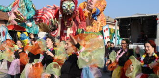 festa di carnevale in piazza con ballerine vestite multicolore e sullo sfondo un carro allegorico