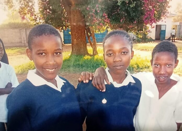 tre ragazzine del Kenya abbracciate tra loro in un bel giardino con un albero fiorito