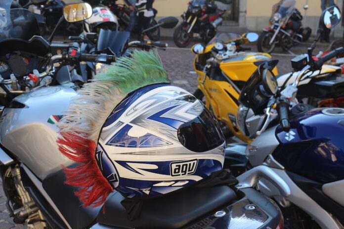 primo piano di un casco con le piume tricolore appoggiato sulla sella di una moto