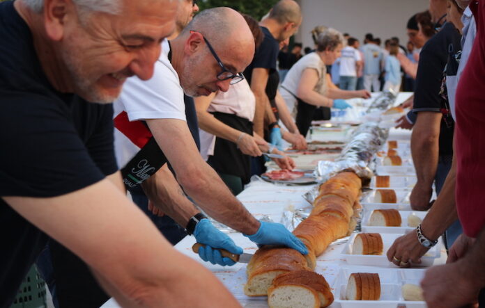 persone lungo una tavolata tagliano il pane