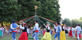 Ballerini in vestiti tipici colorati ballano intorno a un palo tenendo nastri colorati