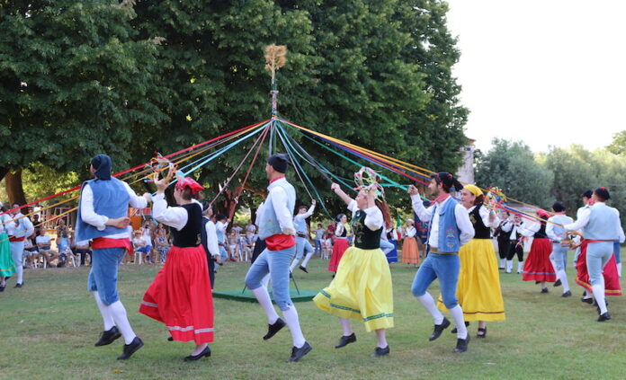 Ballerini in vestiti tipici colorati ballano intorno a un palo tenendo nastri colorati