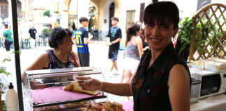 una signora sorridente con una camicia nera presenta un piatto di pesce fritto